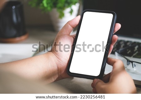 Over shoulder view of woman using mobile phone at her workplace. Blank screen for your advertise design.	