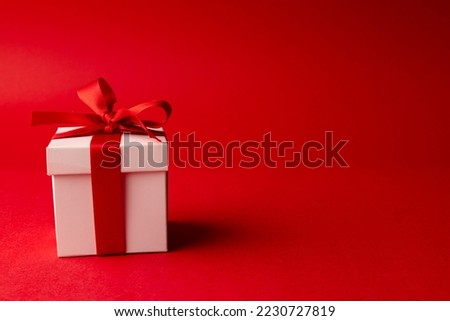 White gift box tied with red ribbon, on red background with copy space. Valentine's day, love, romance and celebration concept.