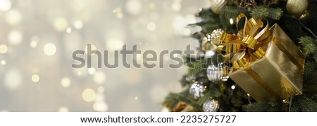 Panoramic banner background Golden Christmas defocused lights gold bokeh with decorated Christmas tree golden gift, balls, green branches. Copy space, selective focus, place for text, mockup 