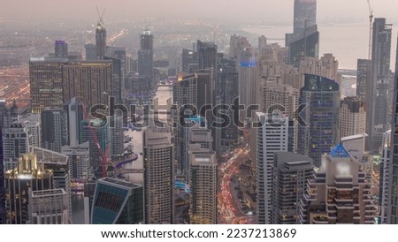 Skyline view of Dubai Marina showing canal surrounded by illuminated skyscrapers along shoreline aerial day to night transition timelapse. Floating yachts and boats after sunset. DUBAI, UAE