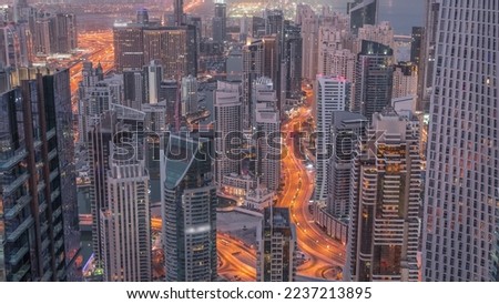 Skyline view of Dubai Marina showing canal surrounded by illuminated skyscrapers along shoreline aerial night to day transition timelapse. Floating yachts and road traffic before sunrise. DUBAI, UAE