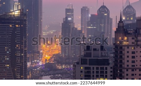 Dubai  and Media City districts with modern skyscrapers and office buildings aerial night to day transition timelapse. Traffic on overpass and road intersection near yachts in harbor