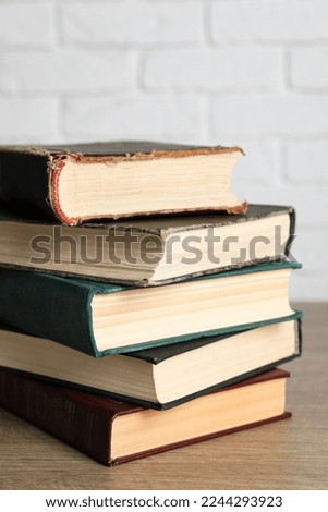 Stack of old hardcover books on wooden table near white brick wall