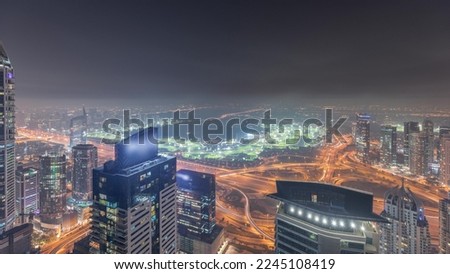 Panorama of Dubai Marina with JLT skyscrapers and golf course night timelapse, Dubai, United Arab Emirates. Aerial view from above towers. City lights illumination