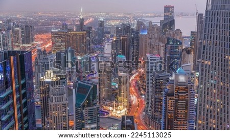 Skyline panoramic view of Dubai Marina and JBR showing canal surrounded by illuminated skyscrapers along shoreline aerial day to night transition. Traffic on curved road after sunset. DUBAI, UAE
