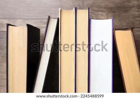 Collection of different books near wooden wall, closeup