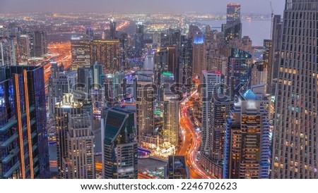 Skyline panoramic view of Dubai Marina and JBR showing canal surrounded by illuminated skyscrapers along shoreline aerial day to night transition . Traffic on curved road after sunset. DUBAI, UAE
