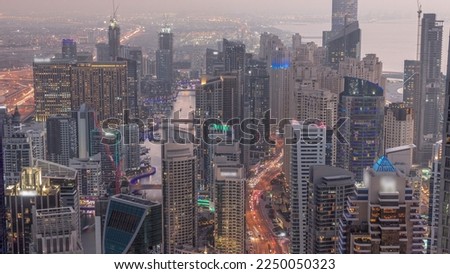 Skyline view of Dubai Marina showing canal surrounded by illuminated skyscrapers along shoreline aerial day to night transition . Floating yachts and boats after sunset. DUBAI, UAE
