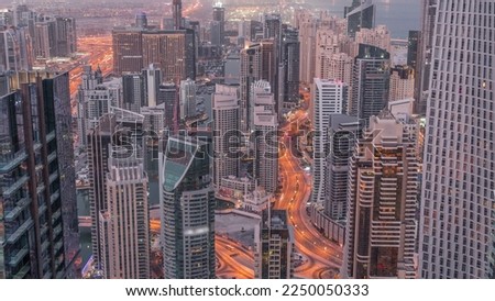 Skyline view of Dubai Marina showing canal surrounded by illuminated skyscrapers along shoreline aerial night to day transition . Floating yachts and road traffic before sunrise. DUBAI, UAE