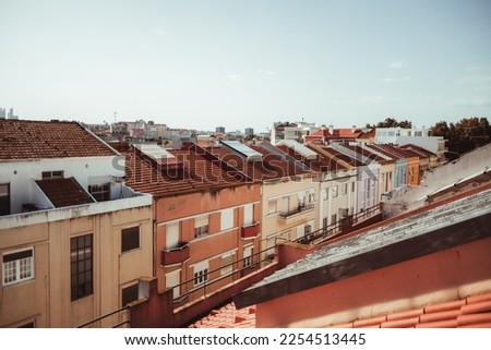 View from the rooftop of a Lisbon residential district with a narrow street full of colorful dwelling houses with clay-tiled rooftops and a cityscape in the background on a sunny day, Portugal
