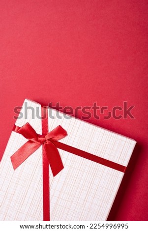 white gift box with red bow on a red background at vertical composition
