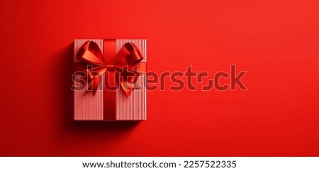 Gift composition. Red striped gift box with red satin ribbon on red background. Flat lay, top view, copy space	