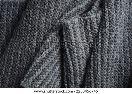 Knitted scarf folds, black and gray stripes. Dark knitted texture background.