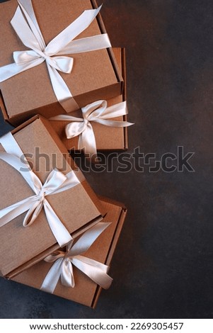 A gift for the holiday. Cardboard boxes on a dark background. Gift delivery. The cardboard holiday box is tied with a ribbon. Festive packaging. With a space to copy. View from above.