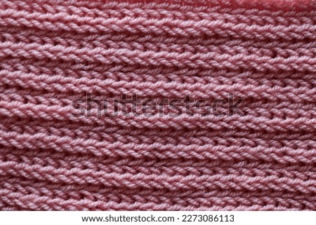 A pink knitted scarf is laying on a bed