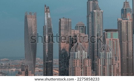 Skyscrapers of Dubai Marina with illuminated highest residential buildings night to day transition . Aerial top view from JLT district. Sun reflected from glass during sunrise