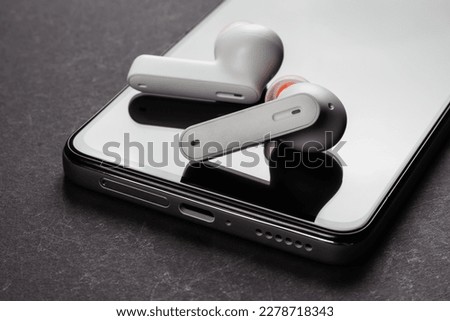 Wirelsss white headphones and smartphone on dark background.