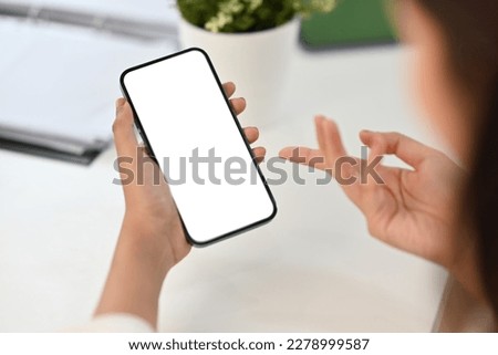 Close up view of woman hand holding smart phone over working desk. White empty screen for app or web site design