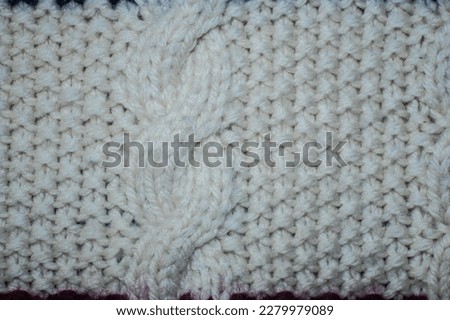 Fragment of an ornament on a knitted woolen sweater. Geometric shapes, lines, waves. Knitted pattern of white threads.