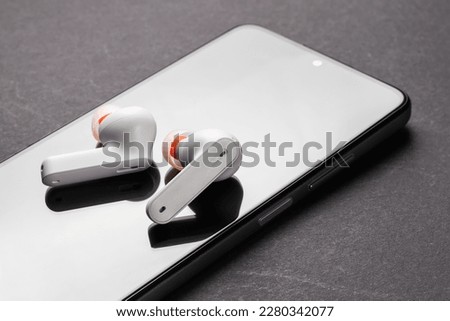 Wirelsss white headphones and smartphone on dark background.
