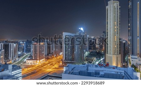 Skyscrapers at the Business Bay in Dubai aerial during all night panoramic with lights turning off. Road intersection and construction site of new towers with cranes, United Arab Emirates