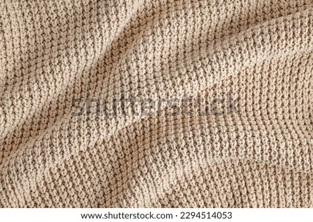 Beige knitted clothes in coarse knit with folds and shadows as a background for design.