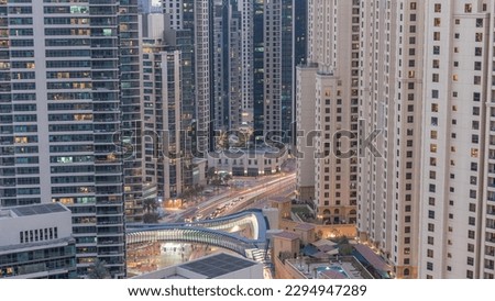 Overview to JBR and Dubai Marina skyline with modern high rise skyscrapers waterfront living apartments aerial day to night transition . Traffic on road intersection and footbridge