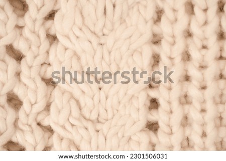 A fragment of beige knitted fabric, knitted from white sheep wool. Knitted background. 