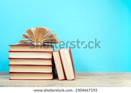 Composition with hardback books, fanned pages on wooden deck table and blue background. Books stacking. Back to school. Copy Space. Education background. Tuition payment.