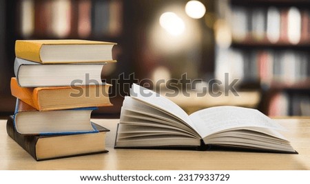 Book stack and opened book on the desk on blurred bookshelves in public library room background