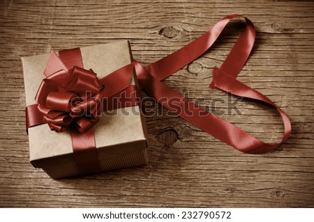 a gift box tied with red ribbon on a rustic wooden table and red ribbon forming a heart, with a retro effect