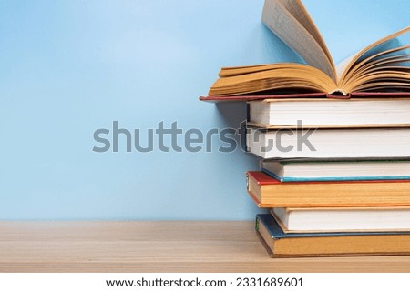 Stack of books in the colored cover lay and open book whith old pages on the wooden  table and blue backround. Education learning concept