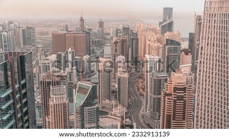 Skyline view of Dubai Marina showing canal surrounded by illuminated skyscrapers along shoreline aerial night to day transition. Floating yachts and road traffic before sunrise. DUBAI, UAE