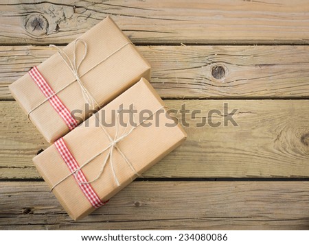two brown paper parcels with red check ribbon against an aged wooden background