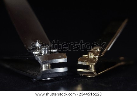Selective blurs on two metal nail clippers isolated on a black background, one white, one gold color. A nail clipper is a manicure tool used to cut and trims nails, mainly fingernails and toenails.