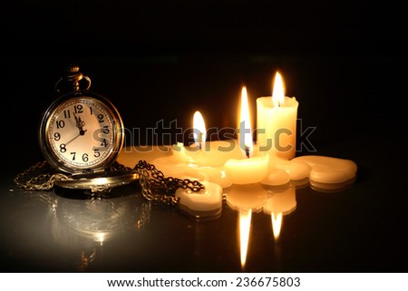 Vintage pocket watch near few lighting candles on dark background