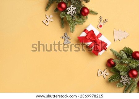 Christmas tree branches with decorations and gift box on yellow background