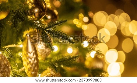 Golden baubles with fairy lights on Christmas tree at home. Holiday ornament with balls and lamp garland on fir tree. Festive decoration with sparkling details and lights on blurry background