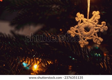 A knitted snowflake is a Christmas tree toy and a symbol of traditional winter holidays. All around is a warm background of shiny layers of a Christmas tree and a green Christmas tree.