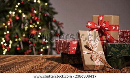 Many gift boxes wrapped in multi-colored paper on a wooden table against the background of a beautiful Christmas tree, copy space. Merry Christmas and Happy New Year greeting concept