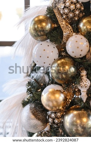 Close-up of a Christmas Tree with White and Gold Glass Holiday Ornaments and White Feathers. Elegant Holiday Decorations.