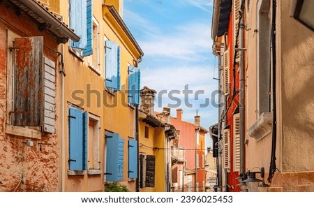 Narrow alley of homes with yellow walls and blue wooden shutters in Roman built town in Croatia.