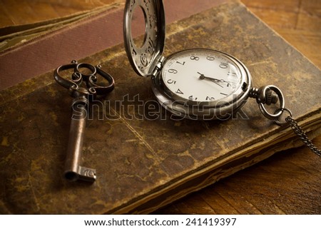 Vintage pocket watch, old book and a brass key on a vintage surface