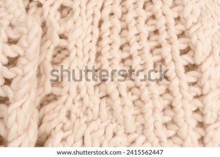 A fragment of beige knitted fabric, knitted from white sheep wool. Knitted background. 