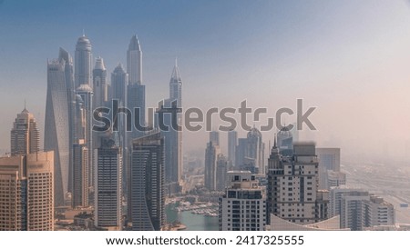 View of various skyscrapers in tallest residential block in Dubai Marina during sunrise aerial timelapse with artificial canal. Many towers and yachts covered by morning fog