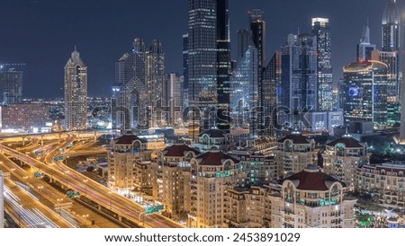 Aerial view of illuminated skyscrapers and road junction in Dubai night timelapse. Traffic on intersection in downtown with modern towers around. Cloudy sky