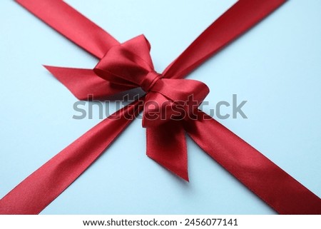 Red satin ribbon with bow on light blue background, closeup
