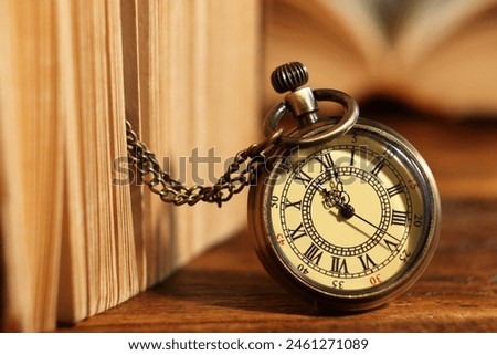 Pocket clock with chain and book on wooden table, closeup