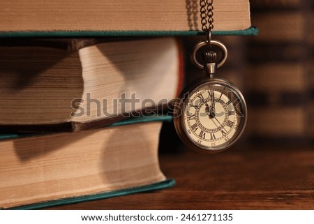 Pocket clock hanging on stack of books at wooden table, closeup