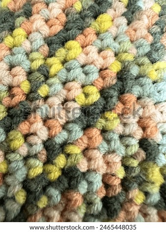 Close-up of a colorful, textured crochet pattern featuring pastel shades of yellow, green, pink, and blue. Ideal for themes of handmade crafts, knitting, and textile design.